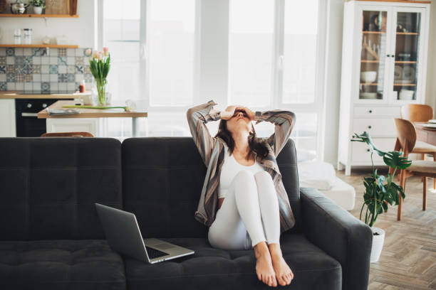 depressed young woman sitting on sofa at home - 悔しい ストックフォトと画像